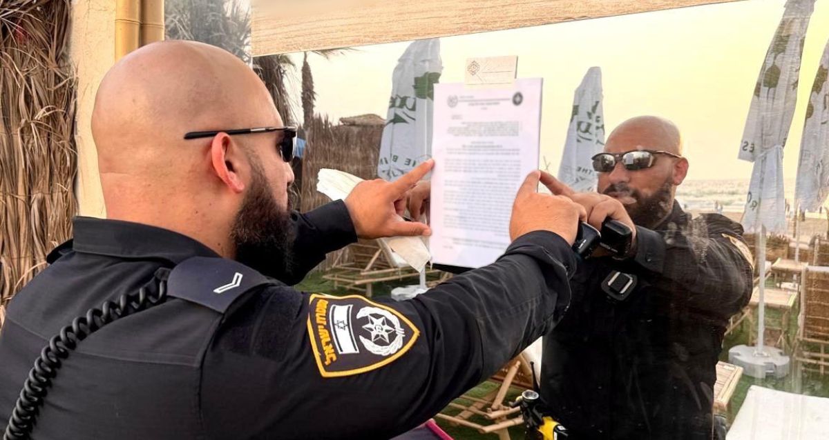 שוטר מדביק צו סגירה על חלון המסעדה. צילום: משטרה