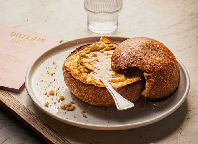 צלחת ועליה קערת מרק מלחם עם מרק בפנים וטוויל גבינה מעל, מכסה עשוי לחן מונח עד הצד, צילום: גליה אבירם